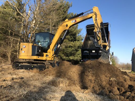 A CAT mini excavator loading soil into a dump trailer on a residential job site